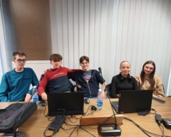 grupa uczniów siedzących za stołem przed laptopami