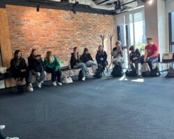 uczniowie siedzący pod ścianą w dużej sali